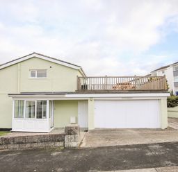 A two-story house with a garage and a wooden balcony with a picnic table at The Little Dolphins in Rhosneigr