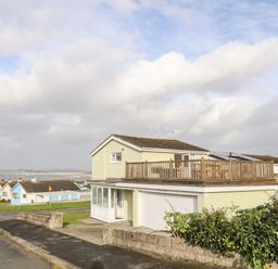 A two story house with a wooden balcony overlooking the sea and a row of smaller houses nearby at The Little Dolphins in Rhosneigr