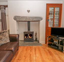 A living room with a leather sofa a fireplace a wooden cabinet and a television on a stand at Oak Tree Cottage in Coniston