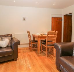 A room with two brown leather armchairs and a wooden dining table with four chairs at Oak Tree Cottage in Coniston