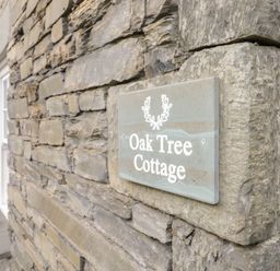A stone wall with a sign that reads Oak Tree Cottage at Oak Tree Cottage in Coniston
