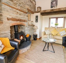 A living room with a stone fireplace a wood-burning stove sofa armchairs and a glass coffee table at Tegfan Barn Pant-y-dwr near Rhayader