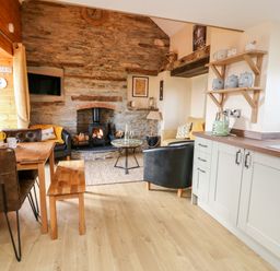 A kitchen and living area with wooden dining table chairs wood burning stove and shelves with jars at Tegfan Barn in Pant-y-dwr near Rhayader