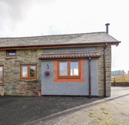 The exterior of a stone and brick house with three windows a tiled roof and a paved driveway at Tegfan Barn Pant-y-dwr near Rhayader