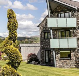 A stone building with glass balconies and a spiral trimmed bush on a grass lawn at The Golf Apartment in Kendal
