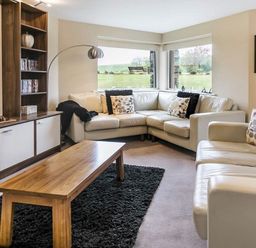 A living room with a wooden coffee table a black rug white sofas and large windows at The Golf Apartment in Kendal