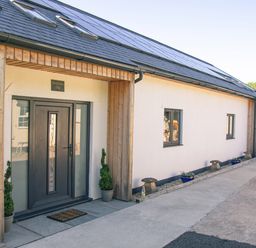 The exterior entrance of a building with a black door and two potted plants next to it at Swallows Dip in Honiton