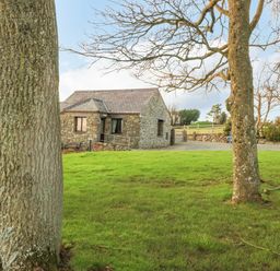 A stone house with a slate roof behind trees and a grassy area at Trem Y Wyddfa in Gaerwen