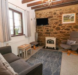 A living room with a grey sofa a grey armchair a blue rug and a wall-mounted television at Trem Y Wyddfa in Gaerwen