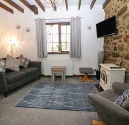 A living room with a sofa armchair small tables rug and a TV on a stone wall at Trem Y Wyddfa in Gaerwen
