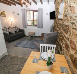 A living room with a gray sofa, armchair, small wooden tables, wall-mounted TV, and a dining table with plates and a plant on it at Trem Y Wyddfa in Gaerwen