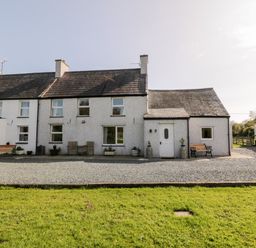 A row of white houses with slate roofs and benches outside on a gravel area at Penllyn in Newborough