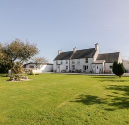 A large grassy yard with picnic table trees and a two-story house with white walls and gray roof at Penllyn in Newborough