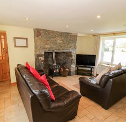 A living room with two brown leather sofas a stone fireplace and a television near a window at Penllyn in Newborough