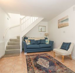 A living room with a blue sofa a beige chair a patterned rug and a staircase at Longships in Porthcurno