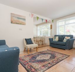 A living room with blue sofas a patterned rug and a small dining table with chairs at Longships in Porthcurno