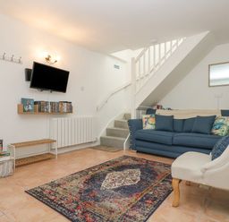 A living room with a blue sofa an armchair a wall-mounted TV and a staircase at Longships in Porthcurno