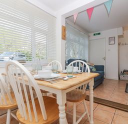 A dining table with four chairs set with bowls and glasses next to a living area with a blue sofa at Longships in Porthcurno