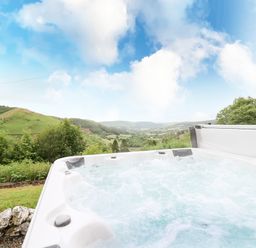 An outdoor hot tub with bubbling water overlooking green hills and trees at Pant Y Rhedyn in Abbeycwmhir near Rhayader