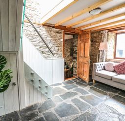 A living room with a gray sofa and cushions near a window a wooden door stone walls and floor at Pant Y Rhedyn in Abbeycwmhir near Rhayader