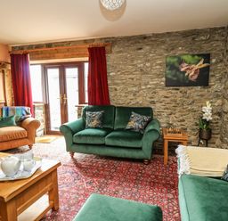 A living room with green and brown sofas a wooden coffee table a chess set and stone walls at Pant Y Rhedyn in Abbeycwmhir near Rhayader