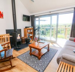 A living room with a wood stove a rocking chair a wooden coffee table and a sliding glass door at Higher Bumsley Barn in Parracombe