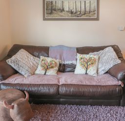 A brown leather sofa with patterned cushions and a throw blanket in a living room at Treetops in Otterburn