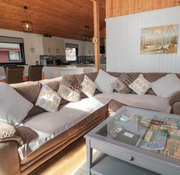 A living room with a large sectional sofa and glass coffee table showing board games with a view into a kitchen with dining chairs at Pine Tree in Otterburn