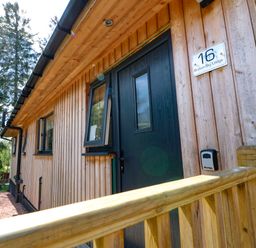 Wooden exterior of lodge with black door and windows near wooden railing at Broken-Sky Lodge in Otterburn