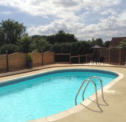 An outdoor swimming pool with a metal ladder surrounded by a wooden fence and trees at Broadclyst Cottage in Ottery St Mary