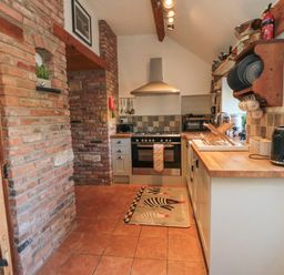 A kitchen with tiled floor wooden countertops and brick walls with shelves holding plates and cups at The Nook at 29 High Street Cloughton near Burniston