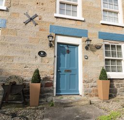 A front entrance with a blue door flanked by two plants in pots at The Nook at 29 High Street Cloughton near Burniston