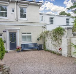 Front yard with a bench and potted plants outside a cream house with a blue door at Barwood View in Torquay