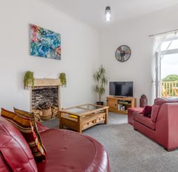 A living room with red leather sofas a wooden coffee table a tv stand with a television and an open door leading to a balcony at Barwood View in Torquay