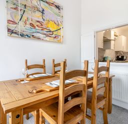 A dining room with a wooden table set for four and an open window to a kitchen at Barwood View in Torquay