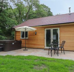 Wooden cabin with a hot tub umbrella and outdoor chairs on a patio at Park Brook Dell in Scorton