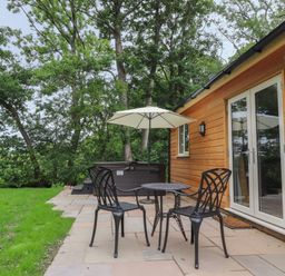 A patio with two black metal chairs a round table and an umbrella next to a wooden house at Park Brook Dell in Scorton