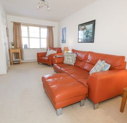 A living room with orange leather sofa and chair beige carpet and wooden side tables at Fairways in Wyke Regis
