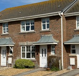A row of brick townhouses with white doors and windows under a blue sky at Fairways in Wyke Regis