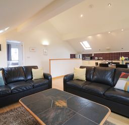 A living room with two black leather sofas and a coffee table next to a kitchen with dining table at Cholwell Barn Apartment Mary Tavy