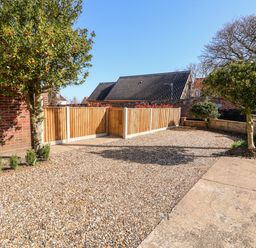 A gravel driveway with two trees near a brick wall and wooden fencing at Sunnyside in Wells-Next-The-Sea