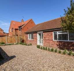 A single-story brick house with a gravel driveway and small plants along the edge at Sunnyside in Wells-Next-The-Sea