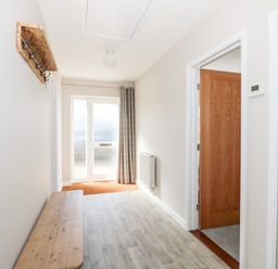 A hallway with a wooden bench and hooks on the wall near a glass door at Sunnyside in Wells-Next-The-Sea
