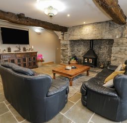 A living room with two black leather sofas a wooden coffee table a stone fireplace with a stove and a wooden cabinet with a television above at Hen Dy Craig Yr Ronwy Capel Celyn near Bala