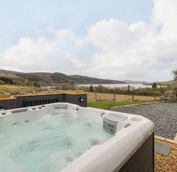 An outdoor hot tub with bubbling water overlooking a grassy field a lake and distant hills at Hen Dy Craig Yr Ronwy in Capel Celyn near Bala