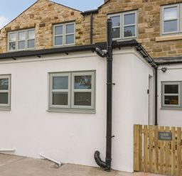 Exterior view of a two-story house with stone upper walls and white lower walls with green framed windows and a wooden fence with a sign saying Holida Hoose in Belford