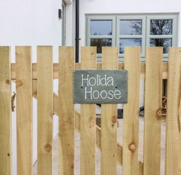 A wooden fence with a sign that reads Holida Hoose and a window on a white building behind the fence at Holida Hoose in Belford