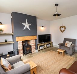 A living room with armchairs a wood burning stove a television and shelves at Holida Hoose in Belford