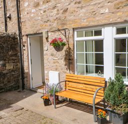 An outdoor area with a wooden bench and potted plants against a stone wall near a door and windows at 1 The Stables in Alston