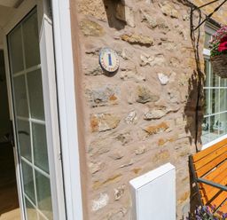 A stone exterior wall with a wooden bench and hanging flower basket at 1 The Stables in Alston